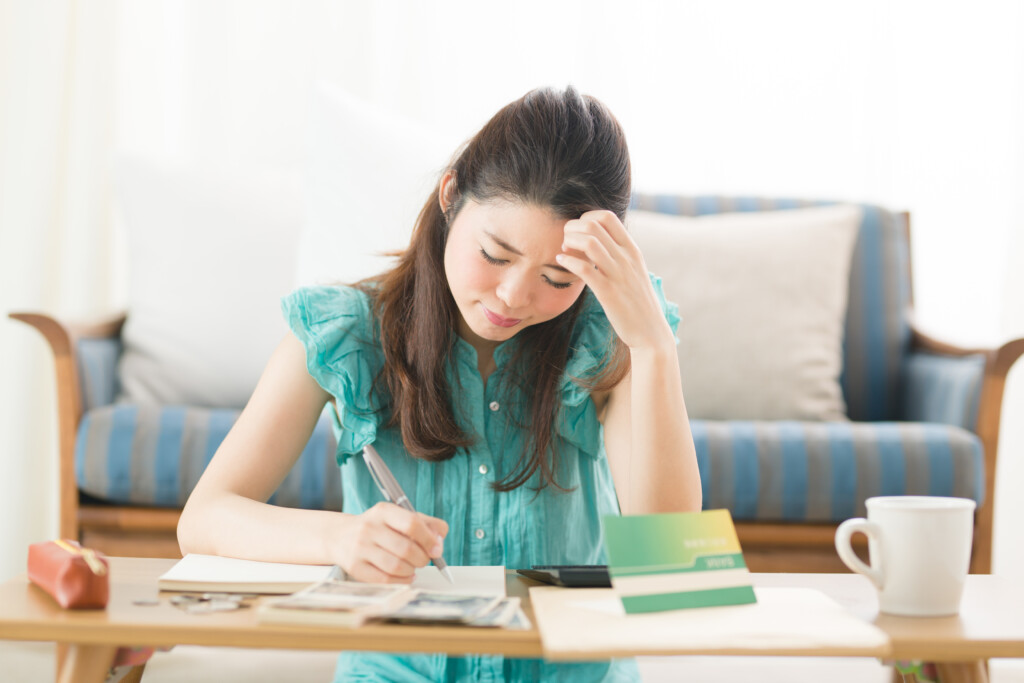 家計簿をつけながら悩む表情の女性