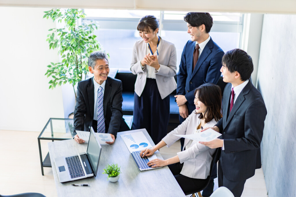 資料を囲んで打ち合わせをするオフィスの社員たち